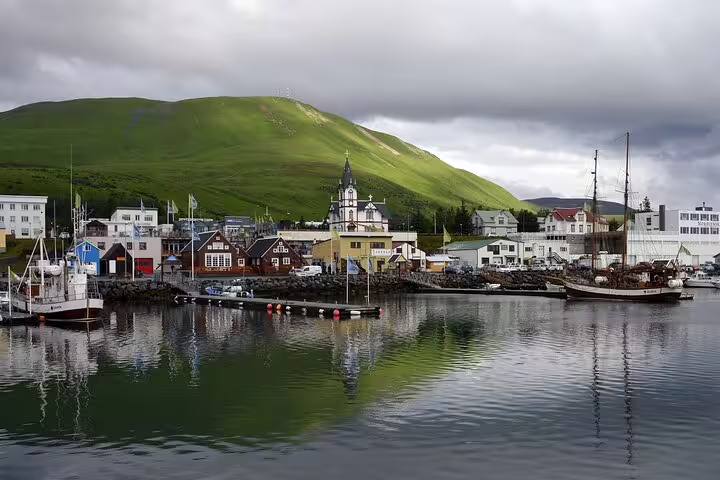 Husavik harbor with colorful buildings, church steeple, fishing boats, and green hillside in North Iceland