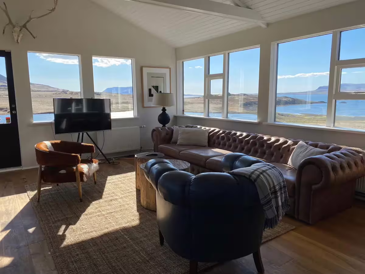 Cozy hidden fjord escape living room with leather sofas and panoramic views of Iceland's serene fjord landscape