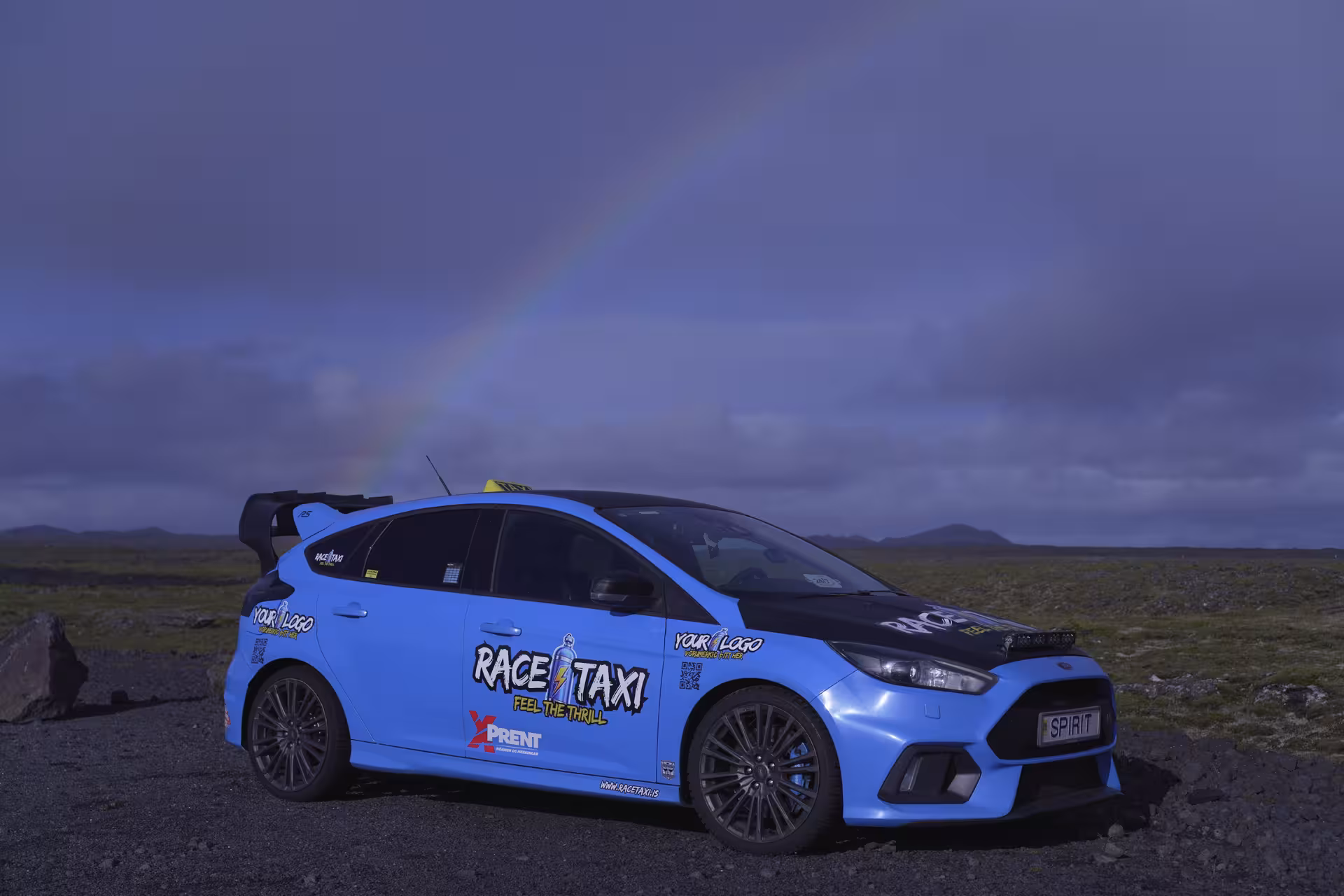 Tour vehicle parked by Hvalfjörður fjord under a rainbow, Iceland scenic drive with optional Hvammsvík baths