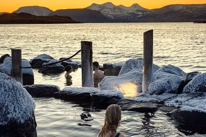 Bathers soaking in Hvammsvik geothermal hot spring at sunset with snow-covered rocks and mountains in Iceland