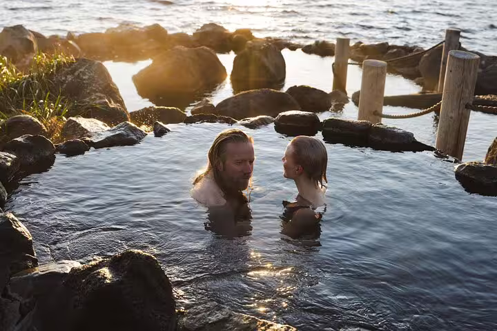 Couple relaxing together in Hvammsvik natural hot spring pool surrounded by rocks at golden hour