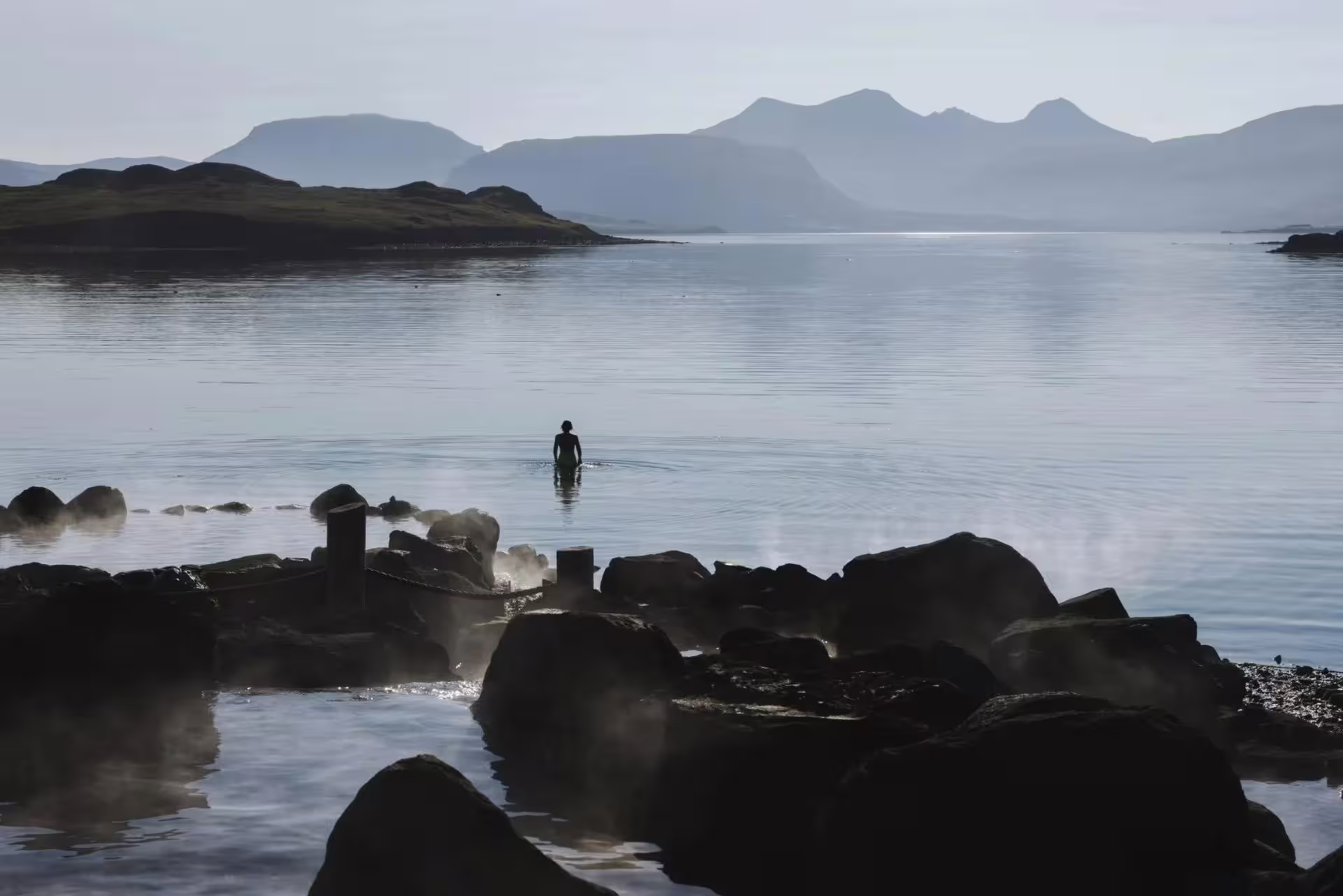 Bather in steaming Hvammsvik Hot Springs by the fjord, relaxing after a private Golden Circle day tour