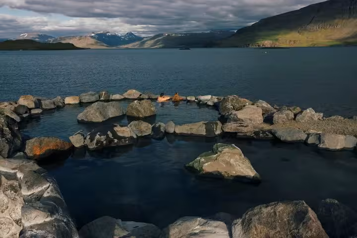 Natural hot spring pool made of rocks overlooking a fjord with snow-capped mountains in Iceland