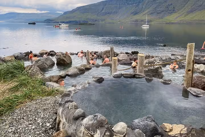Guests soaking in Hvammsvík hot springs natural rock pools with fjord and mountains in background