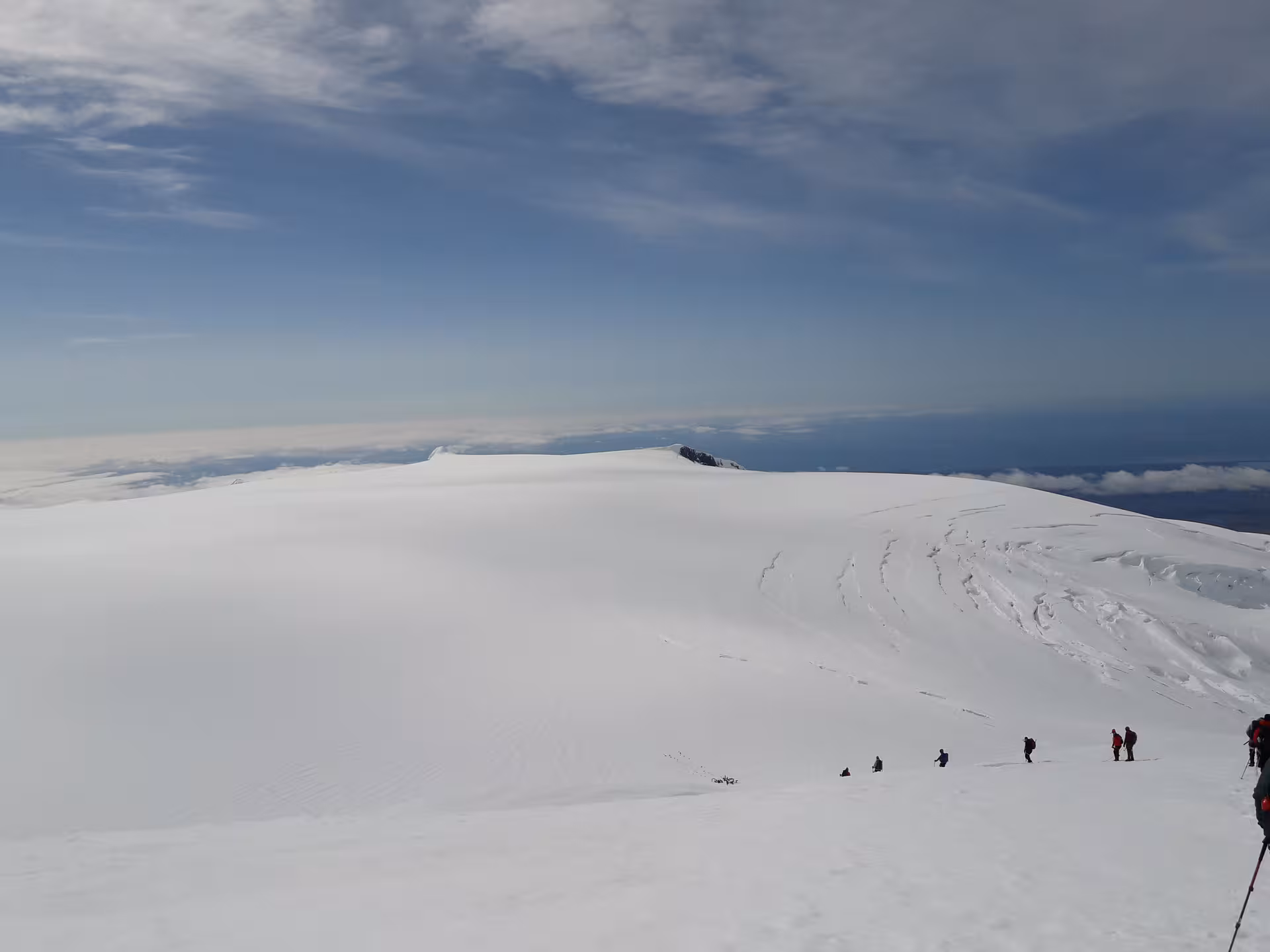 Climbers ascending vast snow-covered Hvannadalshnjukur glacier summit in Iceland under blue sky
