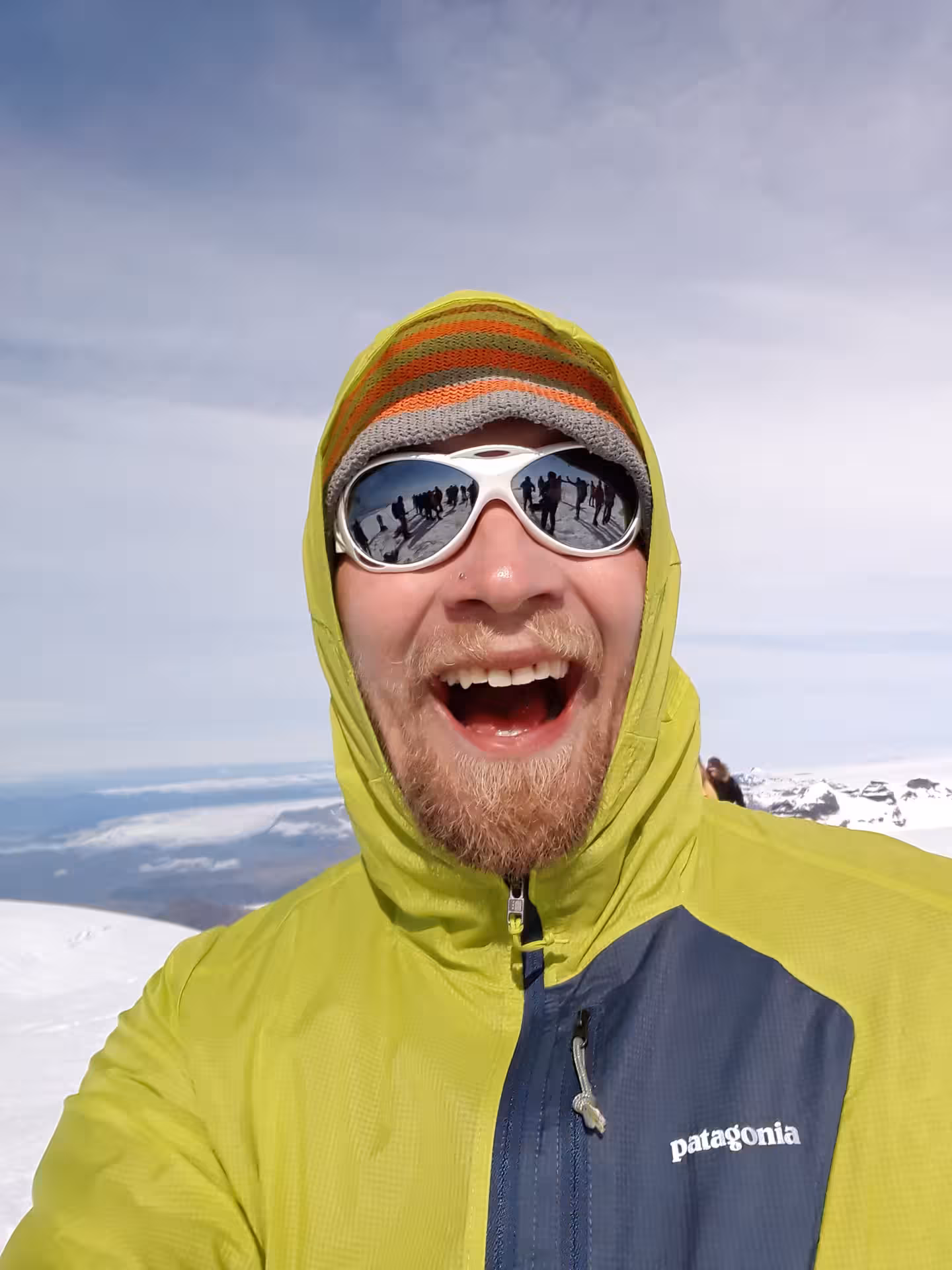 Smiling hiker in yellow Patagonia jacket and ski goggles at snowy Hvannadalshnjukur glacier summit Iceland