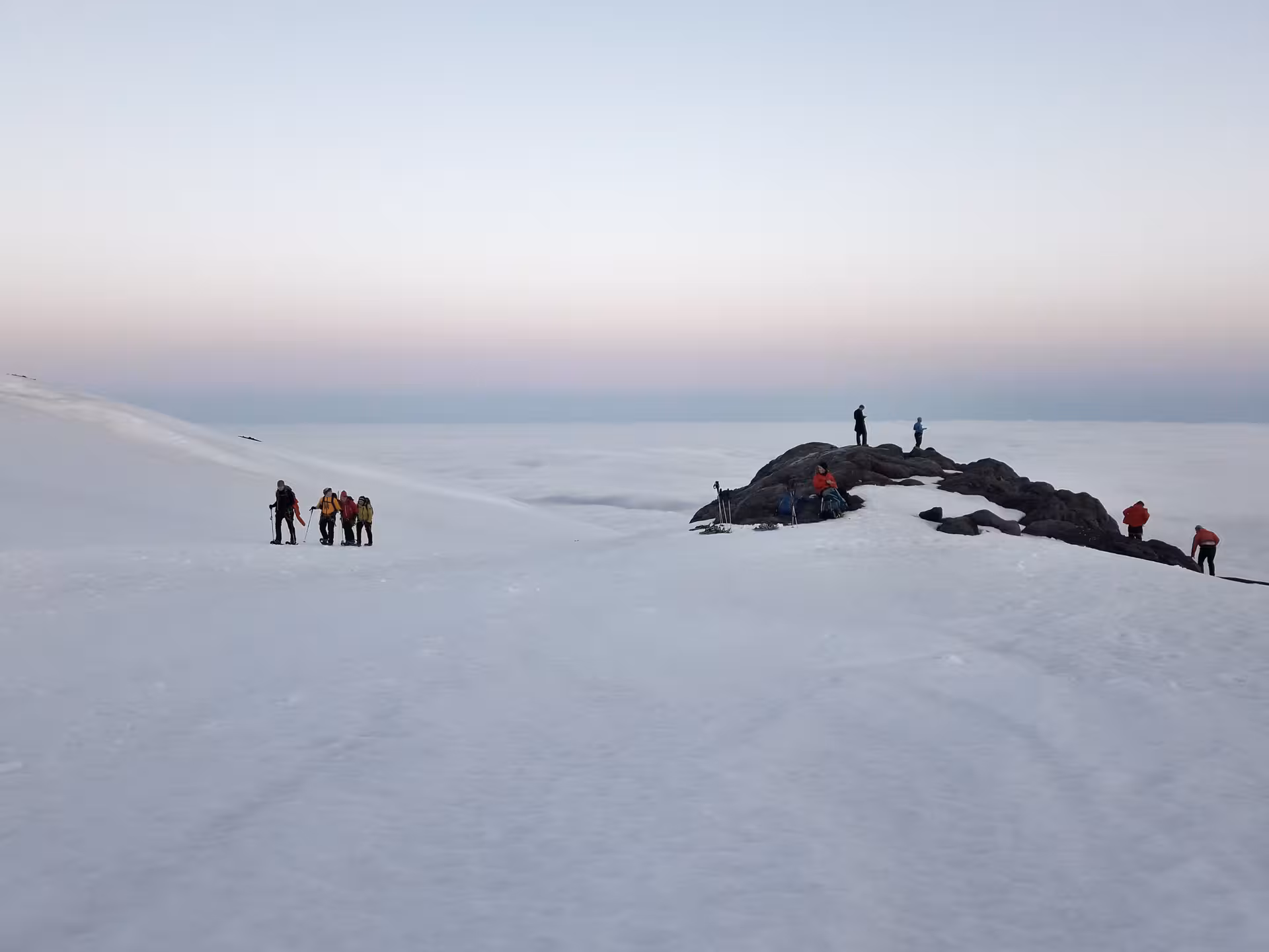 Hikers on snowy Hvannadalshnjukur glacier above cloud layer at dusk, Iceland