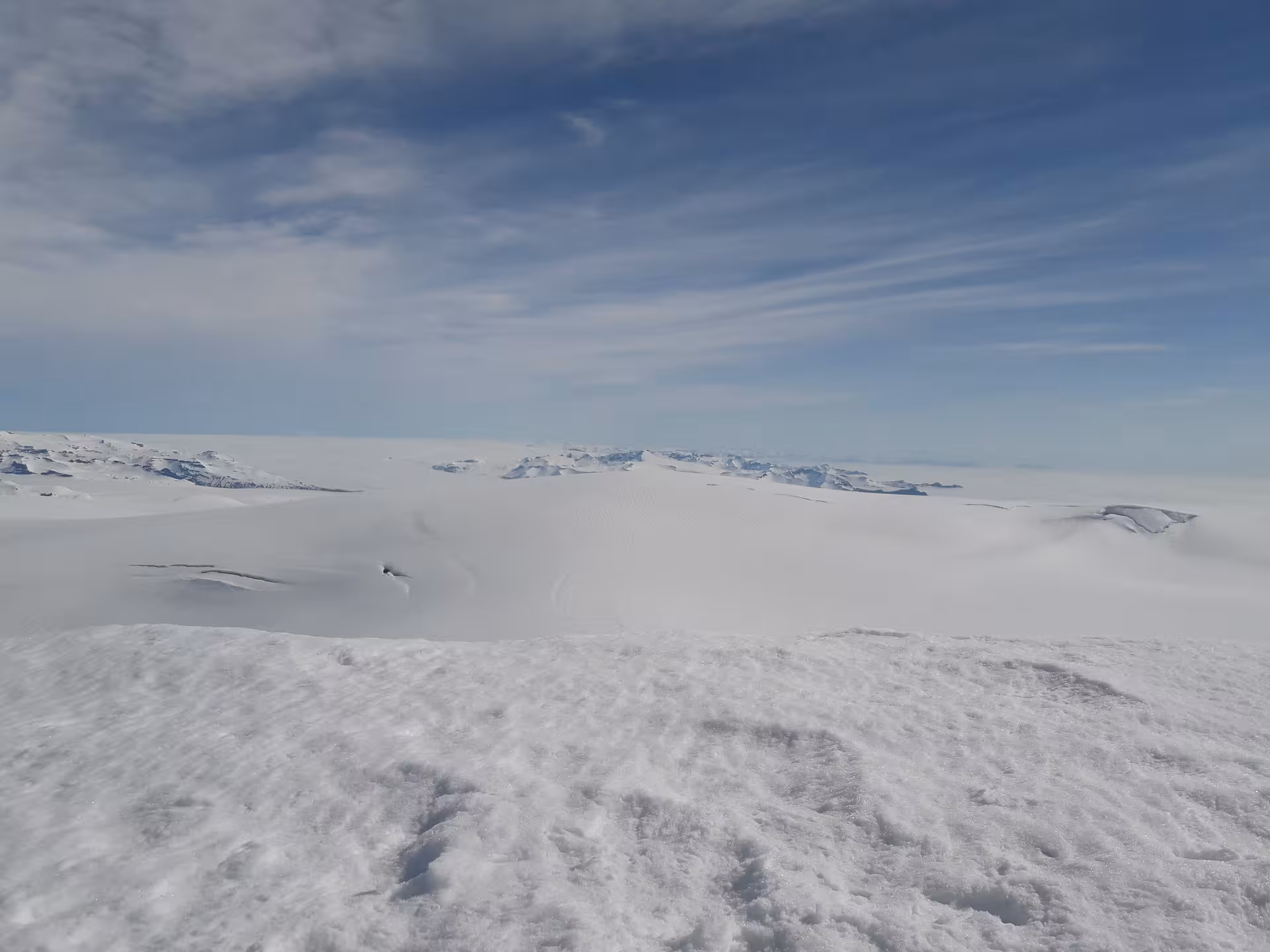Vast snow-covered glacier landscape with distant rocky peaks under blue sky in Iceland