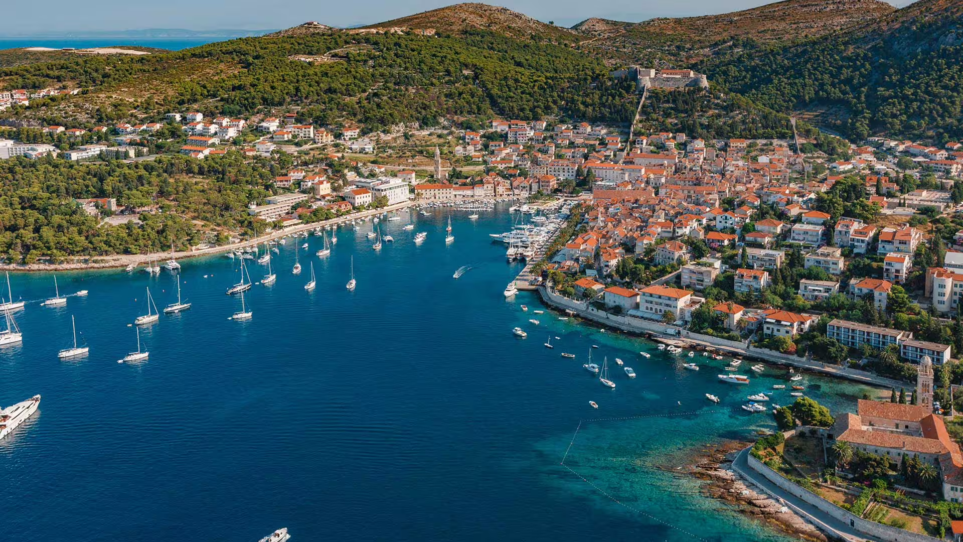 Aerial of Hvar town harbor with yachts and turquoise coves, scenic route on Hvar Brac Pakleni boat tour