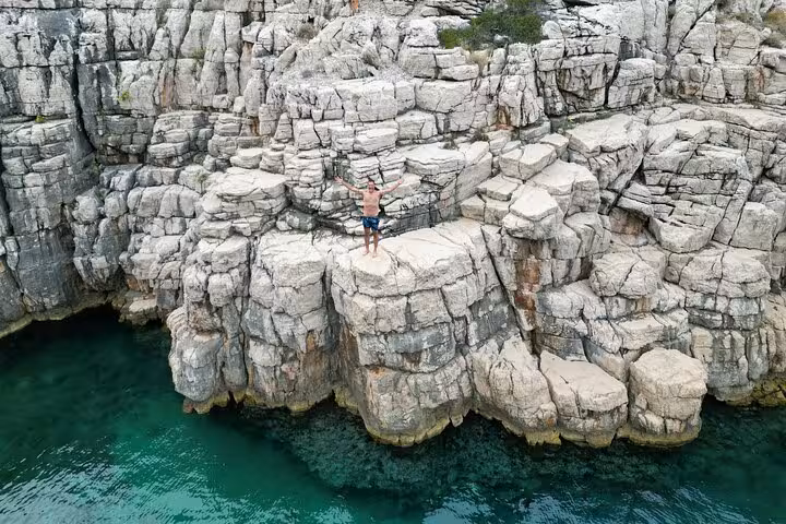 Traveler on rugged limestone cliffs above clear sea on Hvar north shore, Golden Horn private boat tour