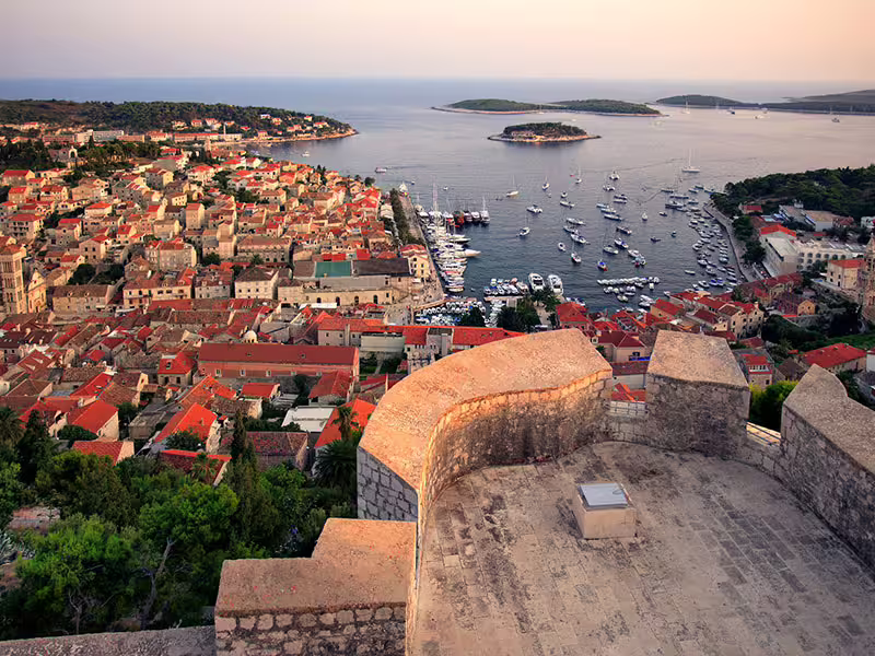 Panoramic Hvar Town harbor view at sunset with yachts and red rooftops, seen from fortress on private boat tour