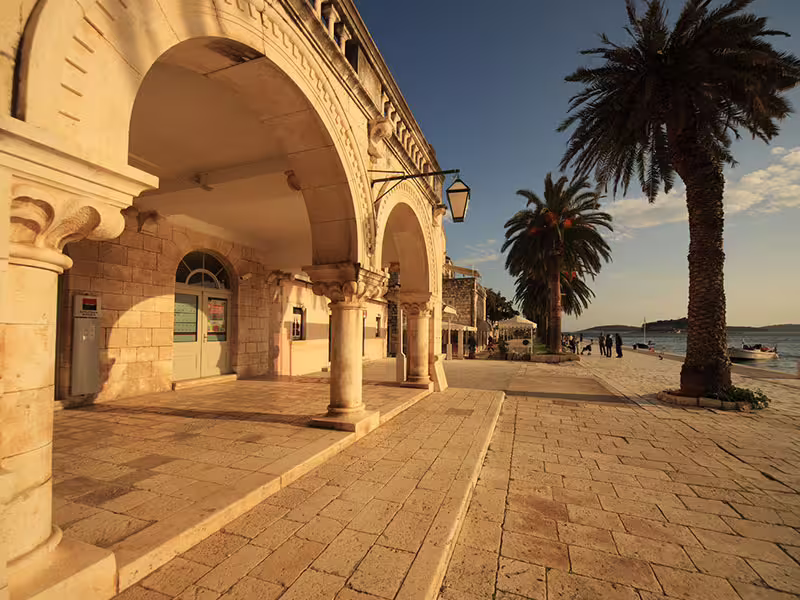 Hvar waterfront promenade with stone arches and palm trees at golden hour, private boat tour Dalmatia