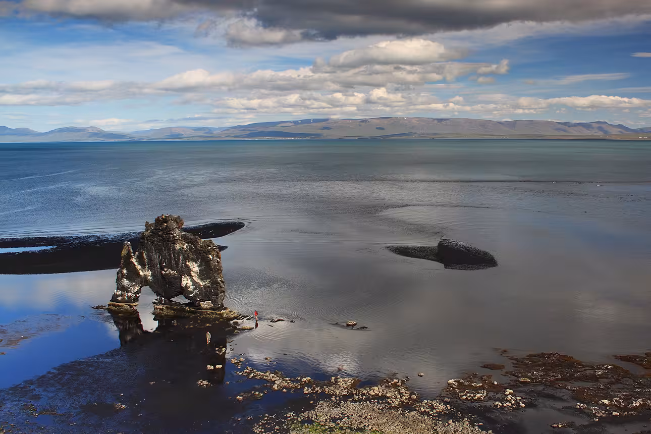 Hvítserkur rock formation rising from calm tidal flats in North Iceland with mountains across the bay