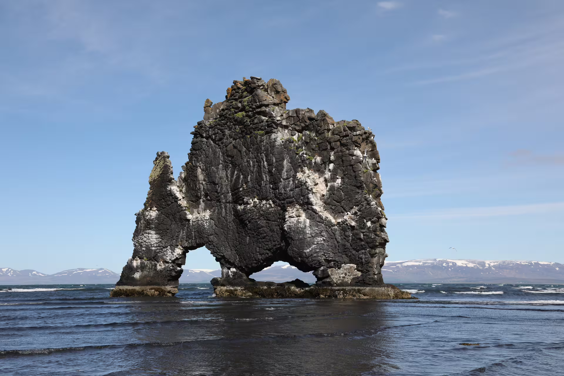 Hvítserkur basalt rock formation rising from the sea in Iceland with snow-capped mountains in background