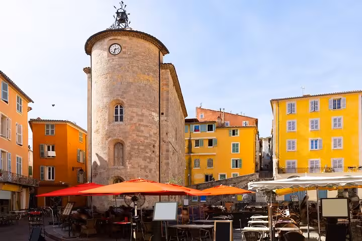 Historic round clock tower surrounded by colorful yellow and orange buildings in Hyères, France