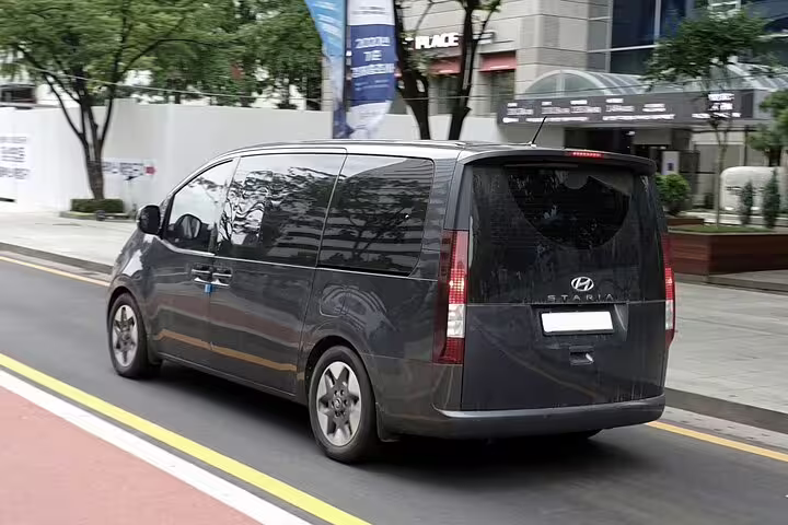 Dark gray Hyundai Staria van driving on city street for private airport transfer