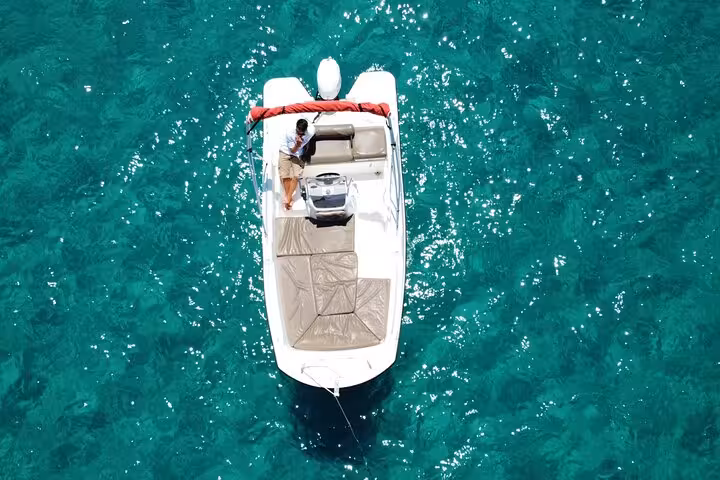 Aerial view of a sleek boat navigating clear turquoise waters, perfect for exploring Ibiza's coastline without a license.