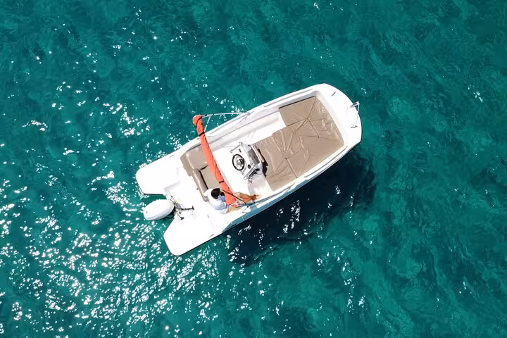 Aerial view of a small white motorboat cruising in Ibiza's turquoise waters, perfect for a license-free boat adventure.