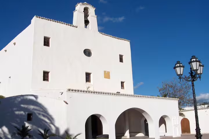 Whitewashed Ibiza church and arches in a sunny village square, seen on island bus tour with official guide