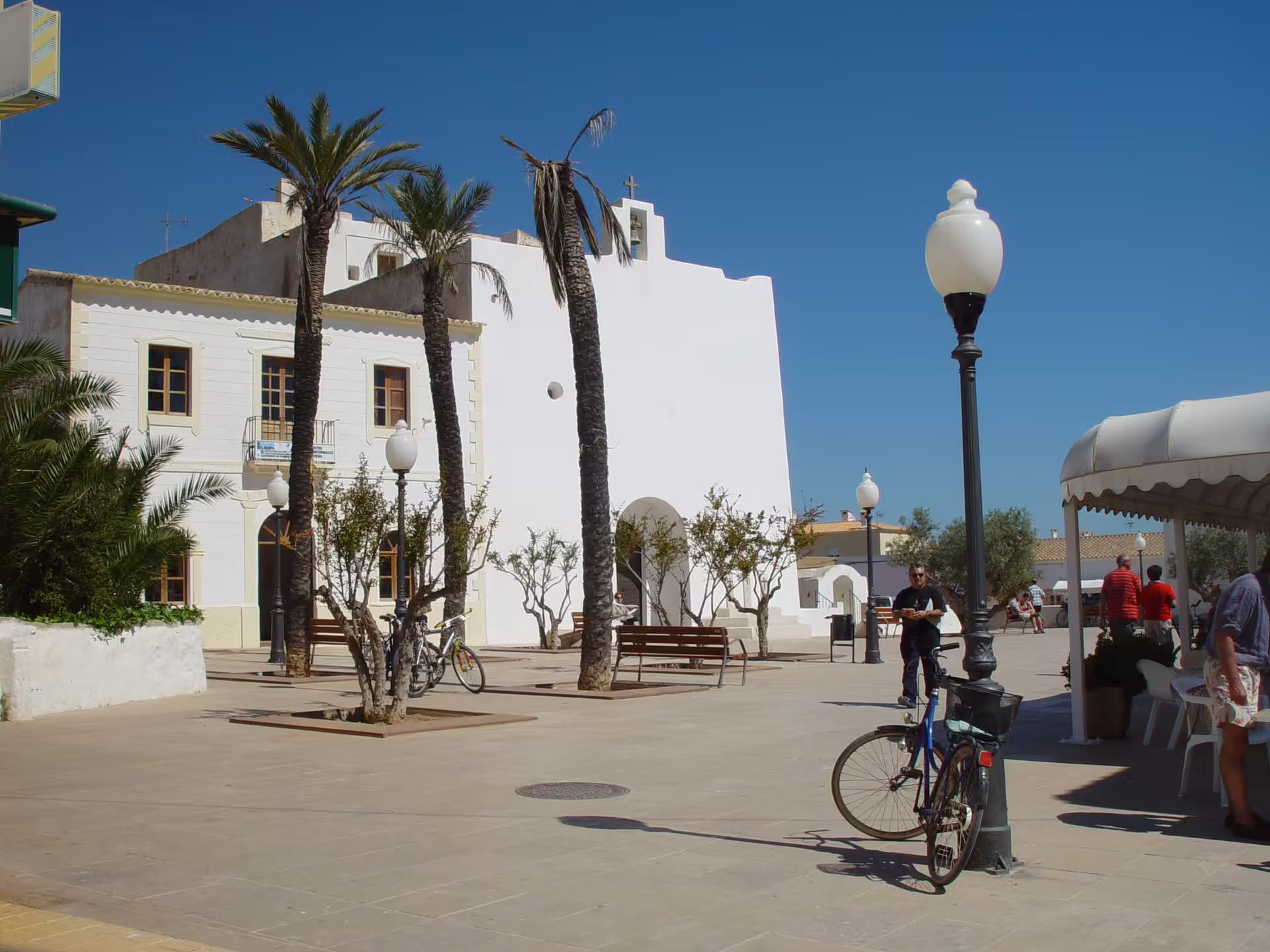 Whitewashed Ibiza village square with palm trees, a church facade, and bikes on the guided bus tour