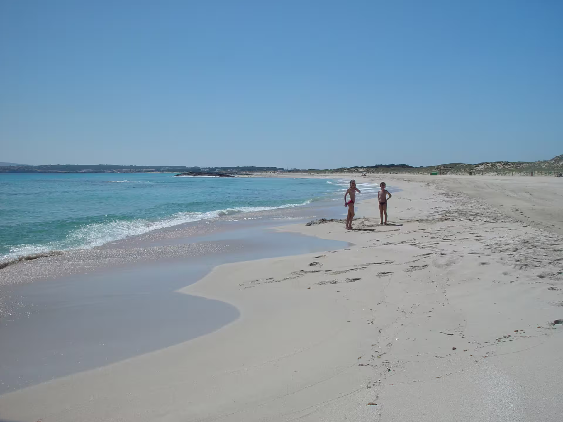 Couple on quiet Formentera shoreline with gentle waves, Ibiza to Formentera fast ferry day trip beach visit