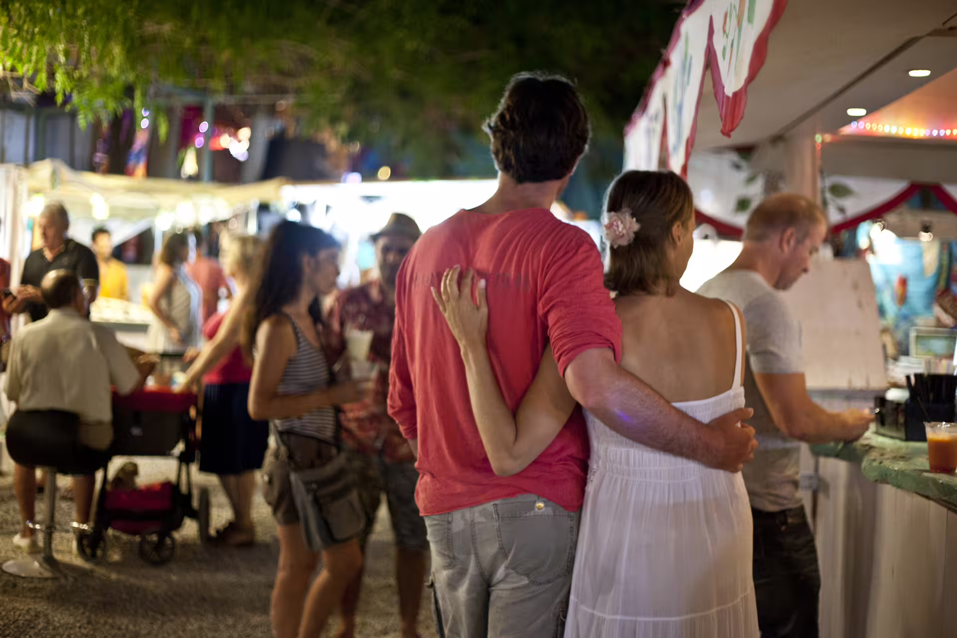 Couple strolling through Las Dalias hippie market at sunset, Ibiza bus tour with lively craft stalls and lights