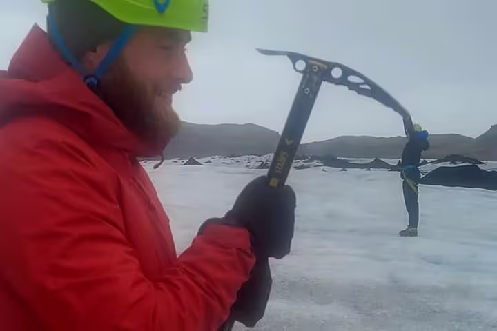 Bearded climber in red jacket holding ice axe on Sólheimajökull glacier with guide in background