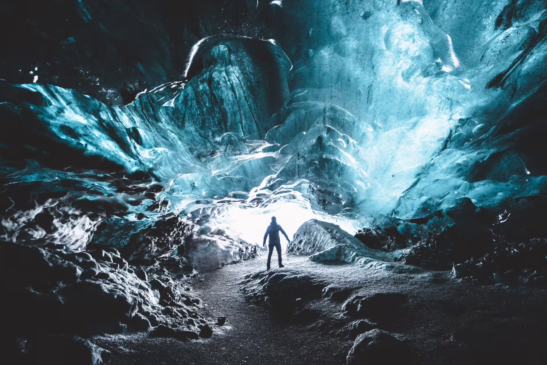 Silhouetted explorer standing inside a glowing blue glacial ice cave with dramatic light