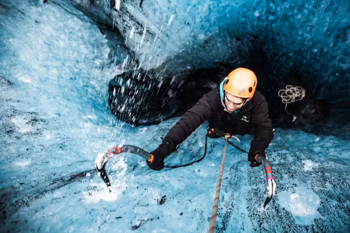 Climber scaling a vivid blue glacial ice wall with ice axes during an ice climbing experience in Skaftafell Iceland