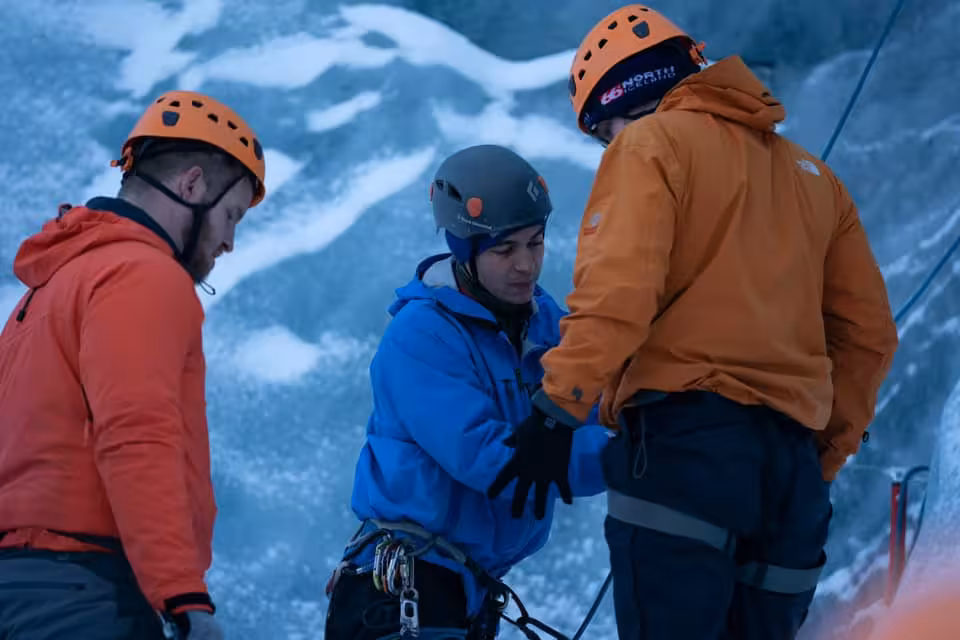 Three climbers in helmets and cold-weather gear preparing equipment on Solheimajokull glacier ice wall