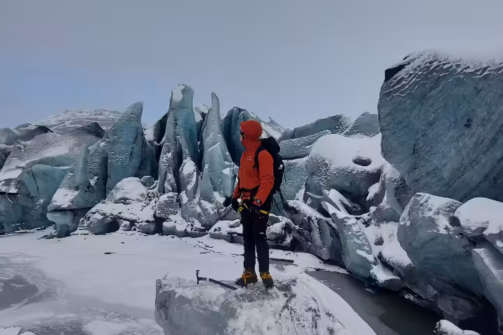 Ice climber in red jacket standing before towering glacier formations in Iceland