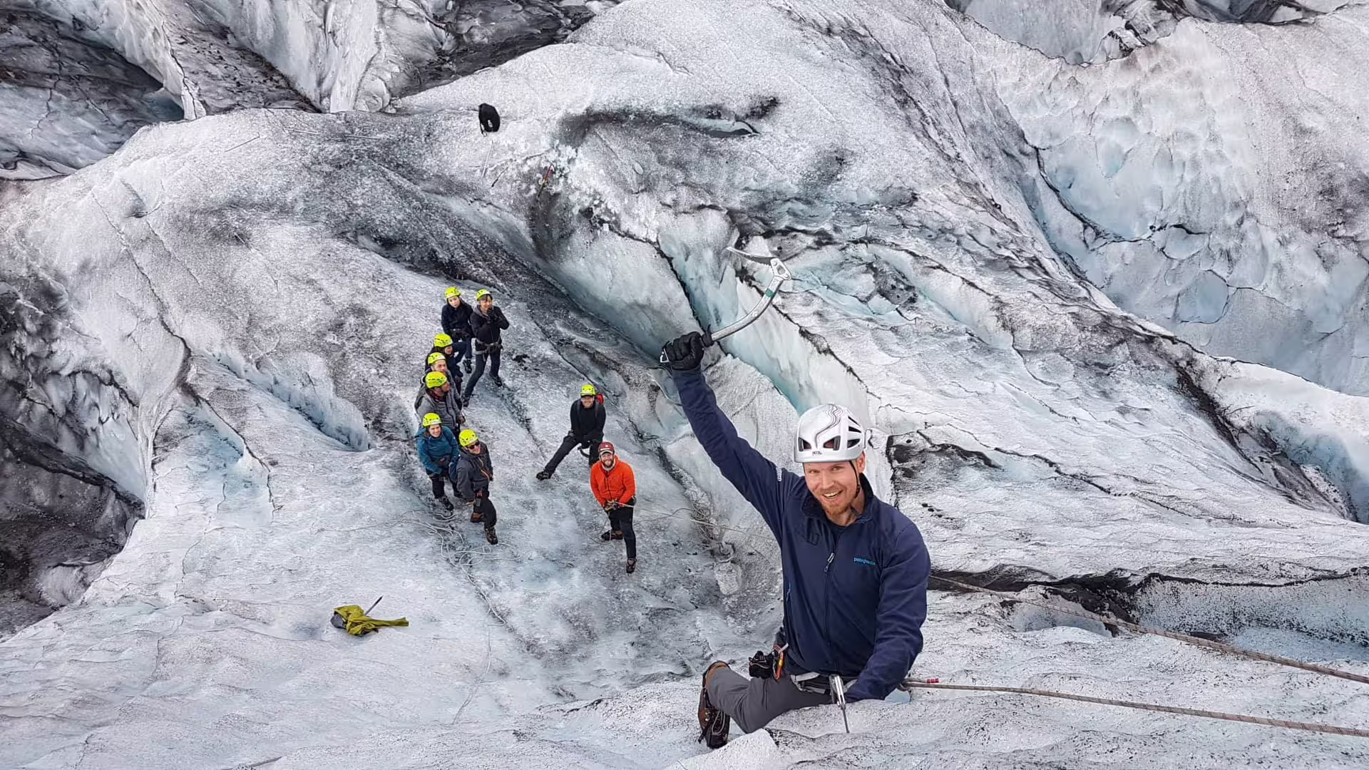 Guide holding ice axe leads group of climbers on glacier ice wall at Skaftafell, Iceland