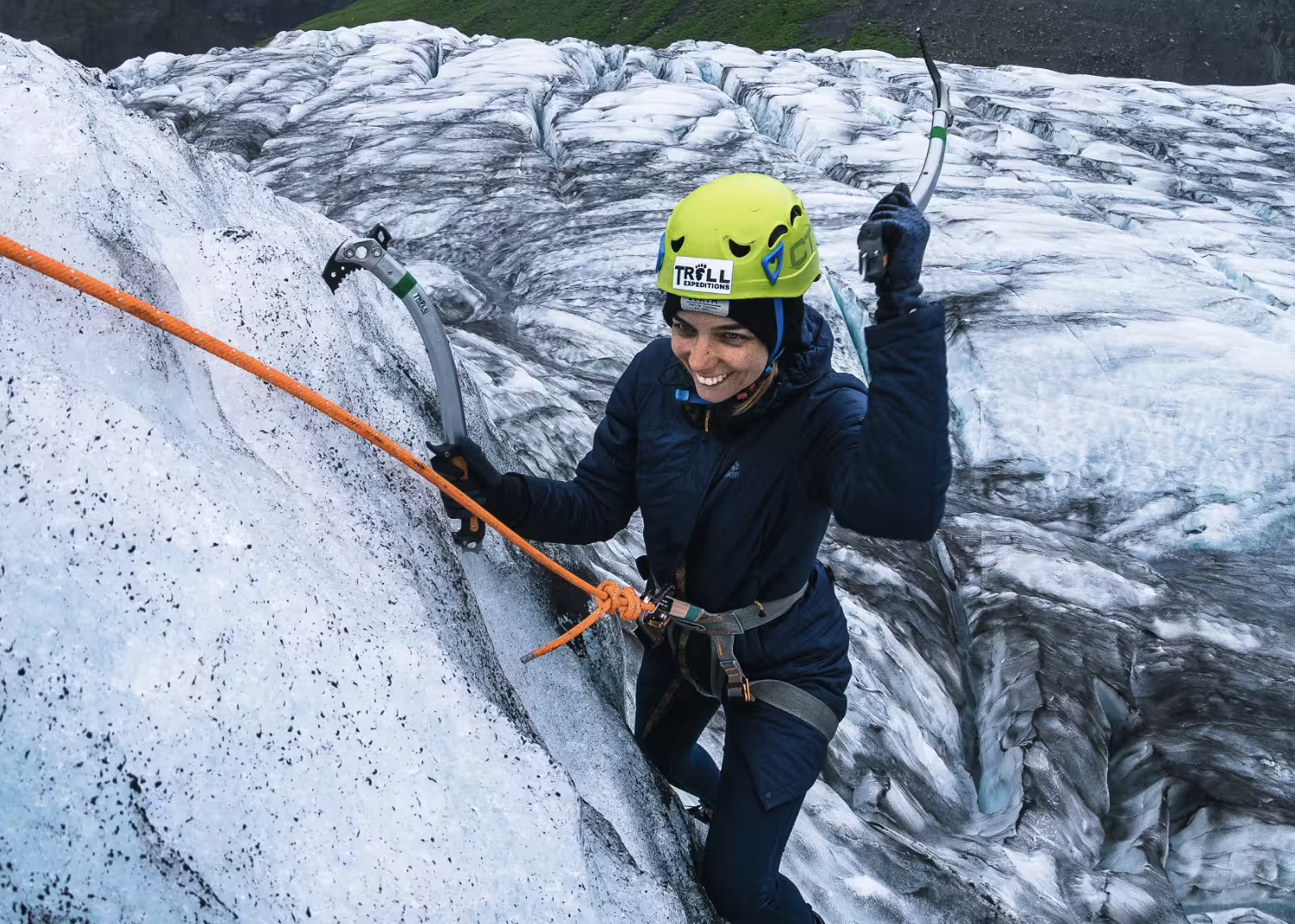 Smiling woman ice climbing on Skaftafell glacier using ice axes and safety harness