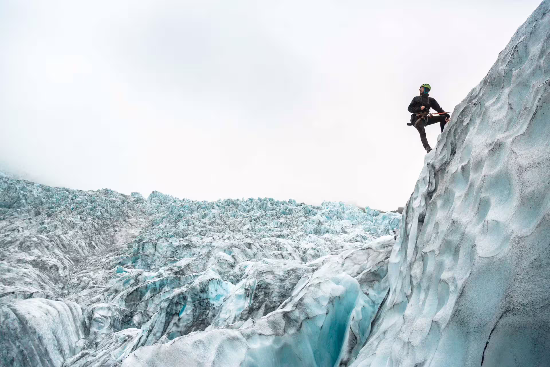 Ice climber with helmet and axes scaling a glacier wall in Skaftafell, Iceland