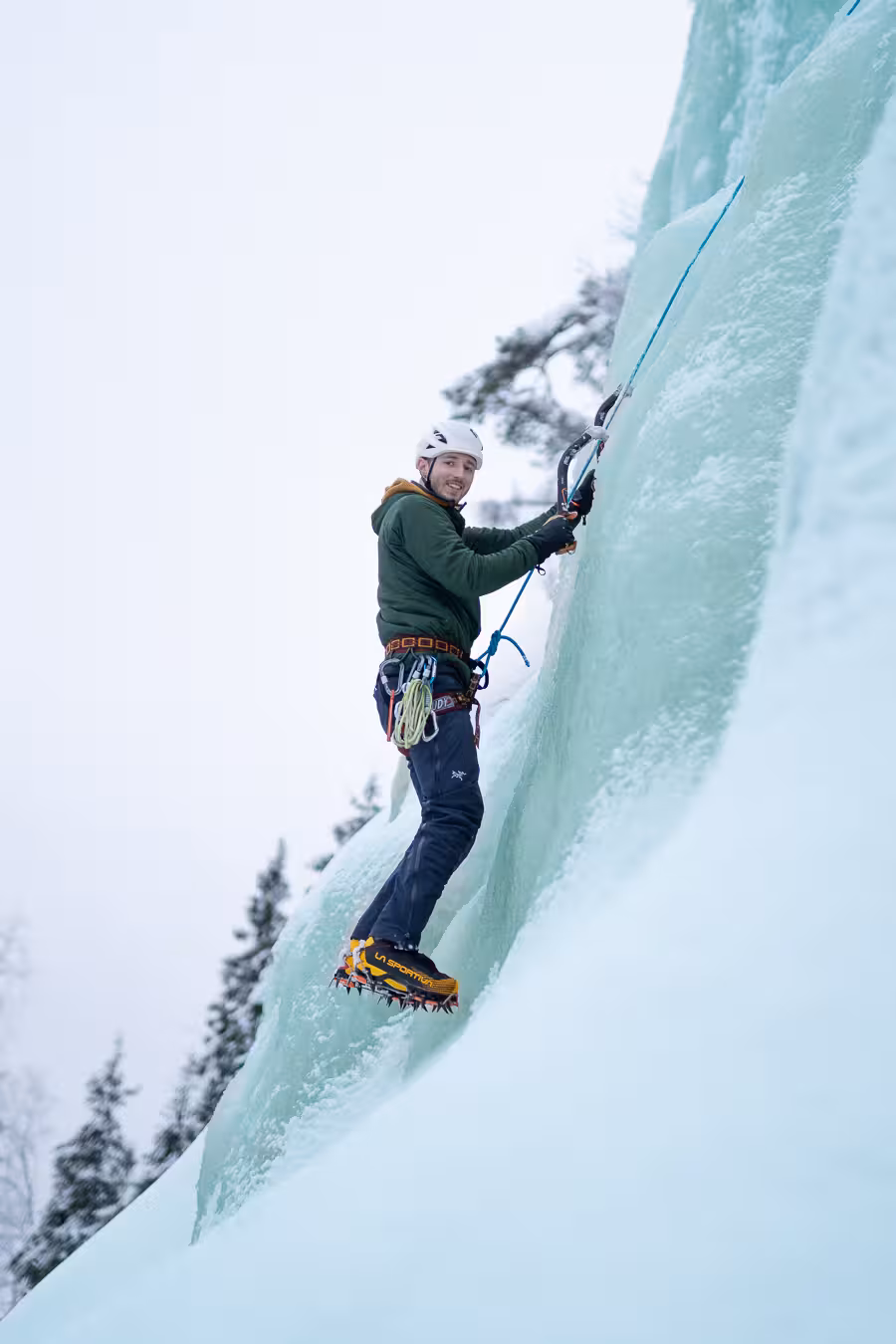 Ice climber ascending a steep, icy cliff in Rovaniemi, Finland, highlighting extreme winter sports excitement.