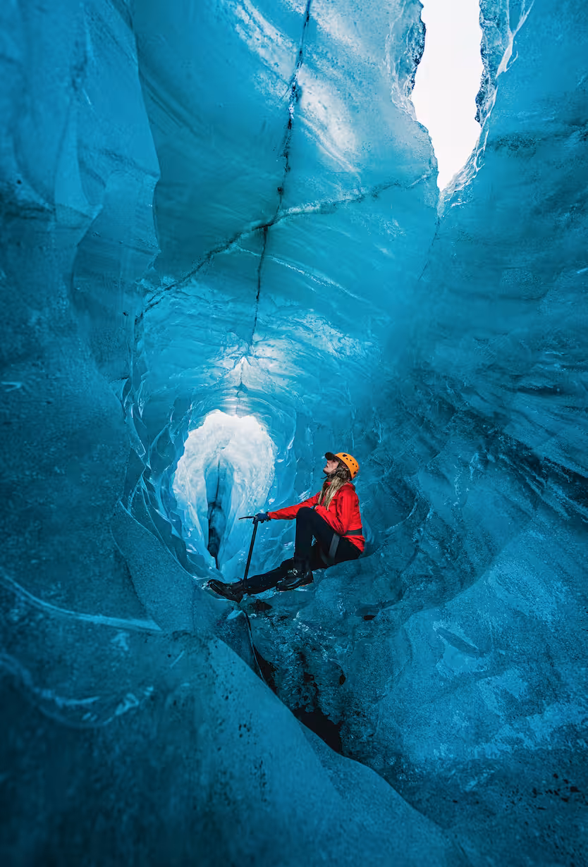 Ice climber in red jacket and orange helmet inside a stunning blue glacial ice cave on Solheimajokull