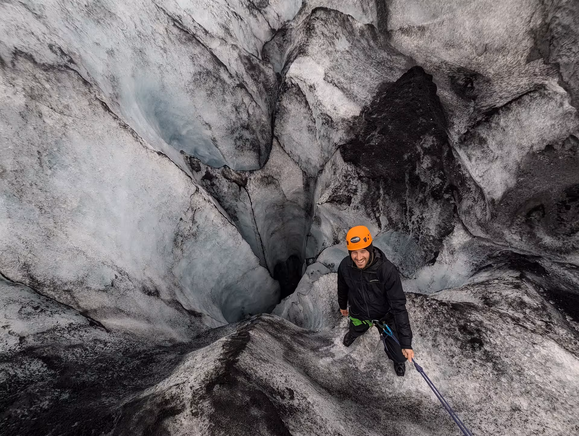 Smiling climber in orange helmet scaling icy glacier wall with rope on Solheimajokull glacier