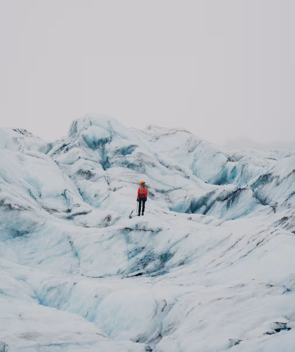 Solo climber in red jacket standing on Solheimajokull glacier ice formations with ice axe