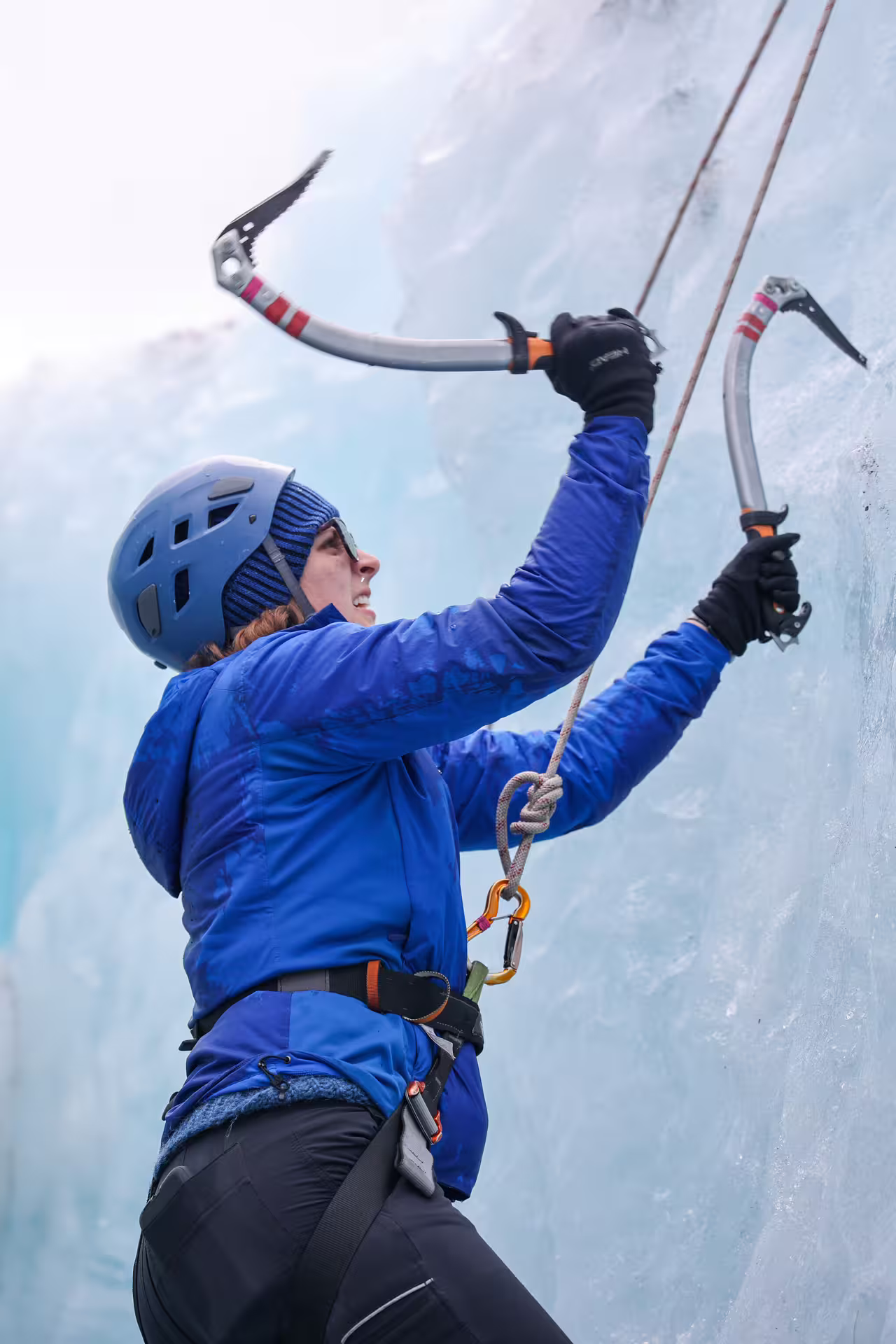 Guided ice climber using dual ice axes and harness to ascend a vertical glacier wall on Solheimajokull Iceland