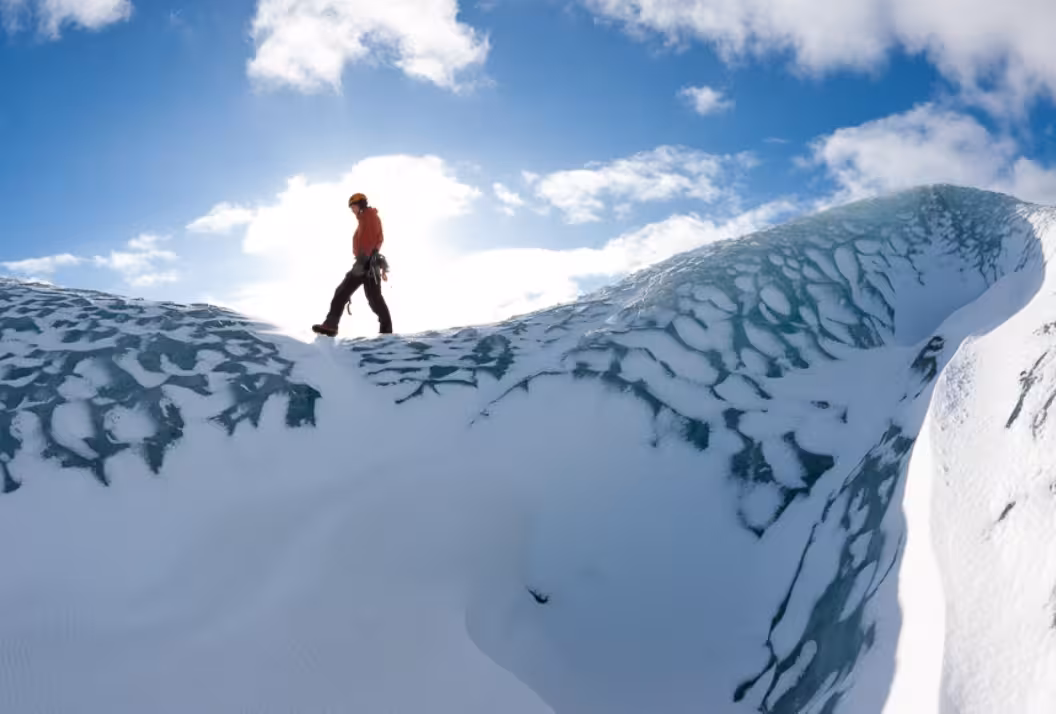 Climber walking along the icy ridge of Solheimajokull Glacier under a blue sky