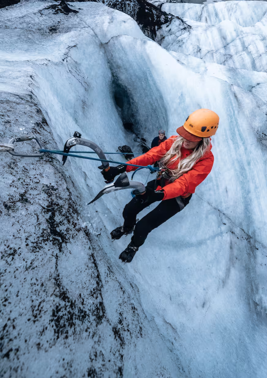 Woman in red jacket ice climbing on Solheimajokull glacier using ice axes and safety rope