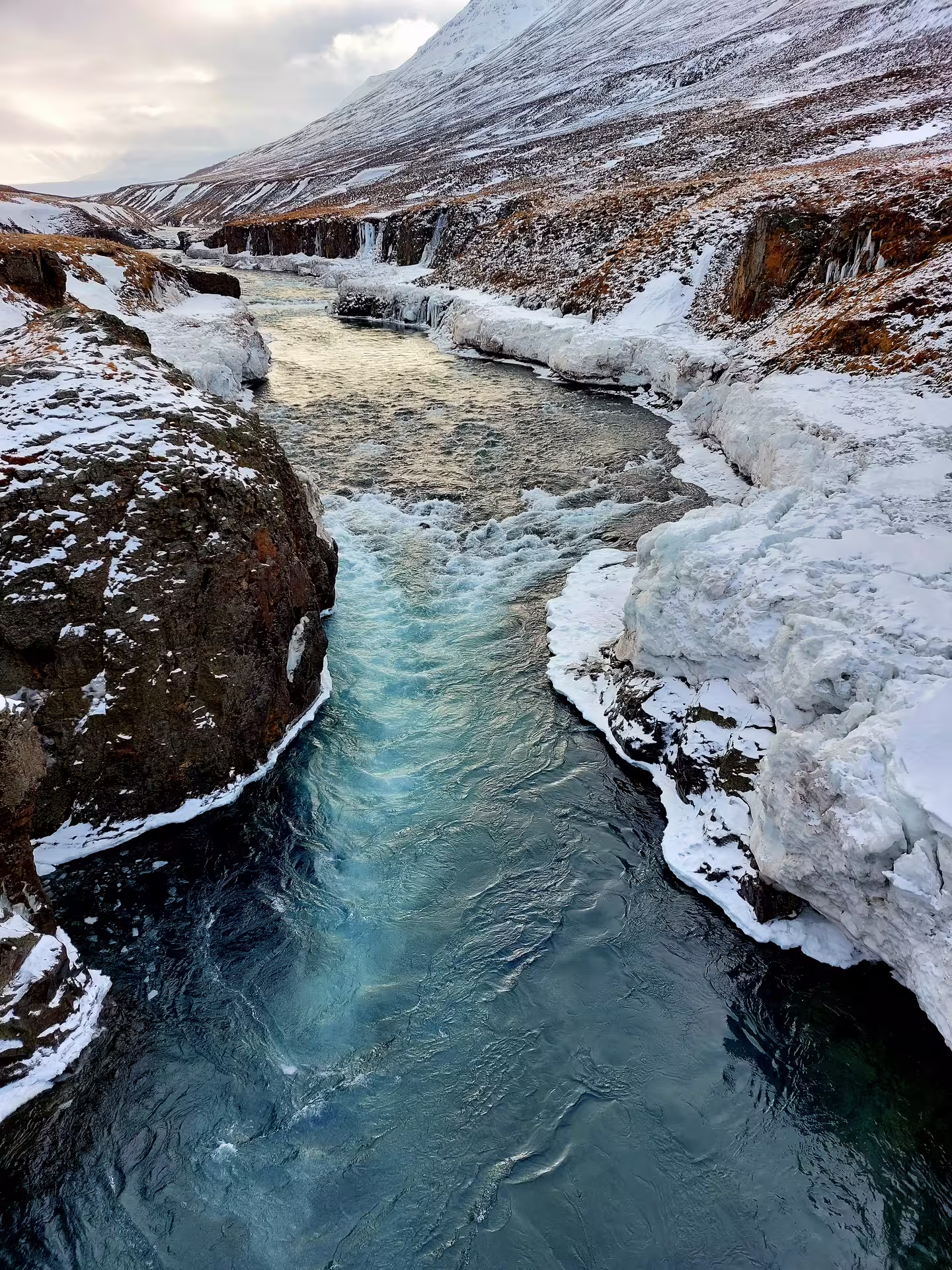 Turquoise glacial river flowing through snow-covered rocky canyon in Akureyri, Iceland in winter