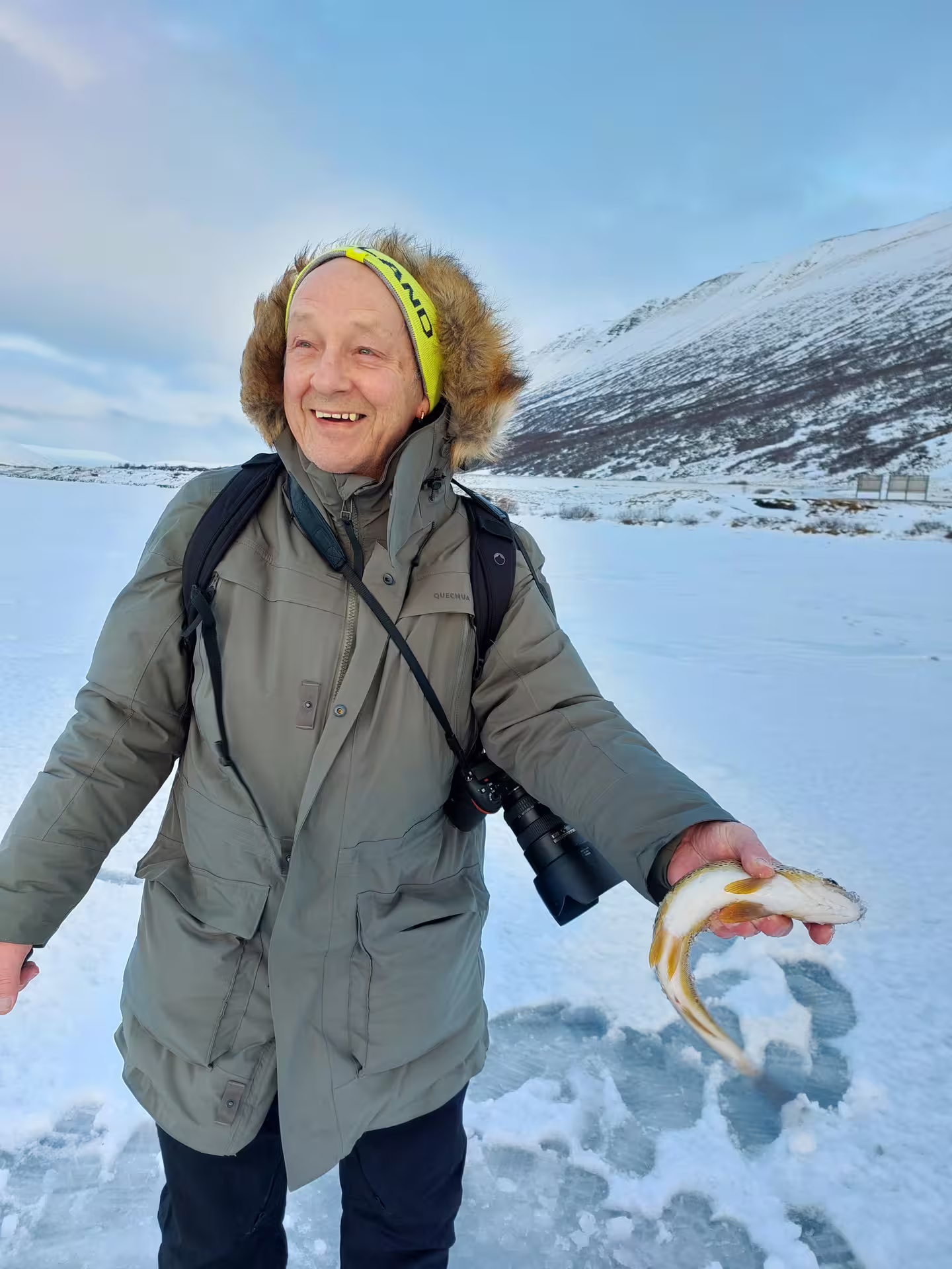 Smiling man holding freshly caught fish during guided ice fishing tour in snowy Akureyri landscape