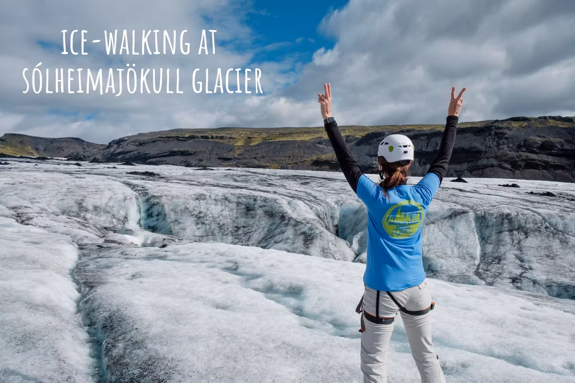 Hiker celebrating with peace signs on Sólheimajökull glacier, Iceland, wearing helmet and harness