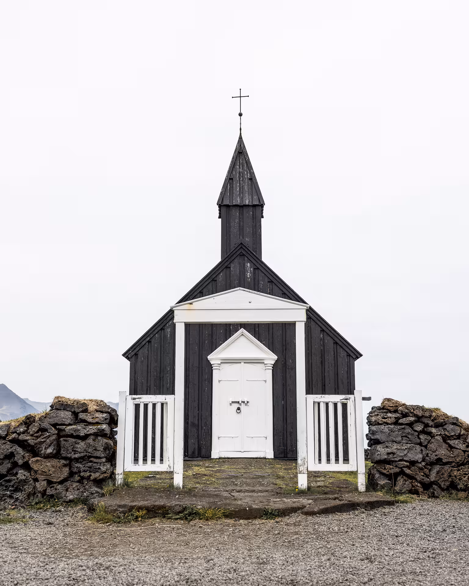 Black wooden Búðakirkja church with white door and cross steeple in Iceland on overcast day