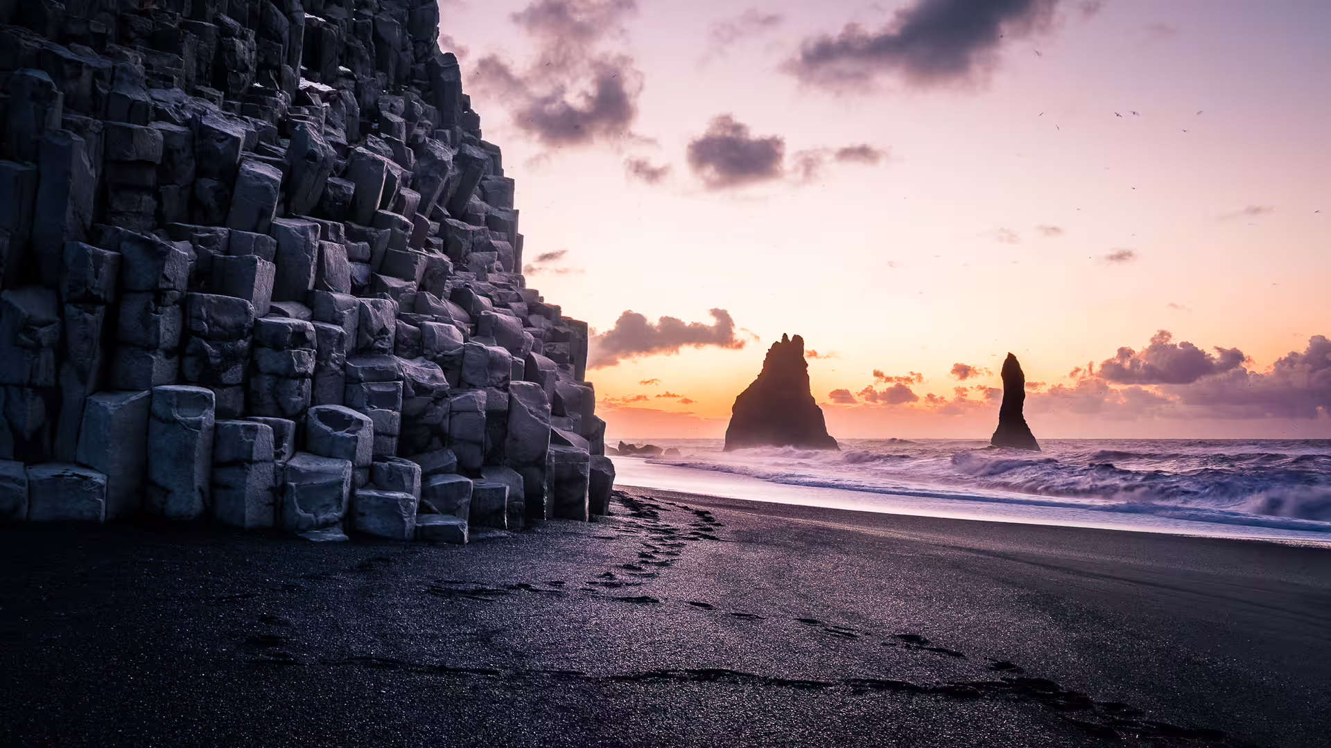 Black sand beach with basalt columns and sea stacks at sunset in Iceland