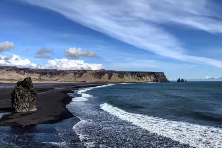 Black sand beach with rock formations and cliffs along Iceland's dramatic coastline under blue sky