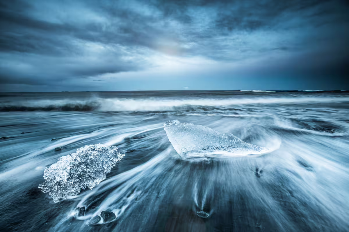 Ice chunks on black sand beach with ocean waves and dramatic cloudy sky in Iceland