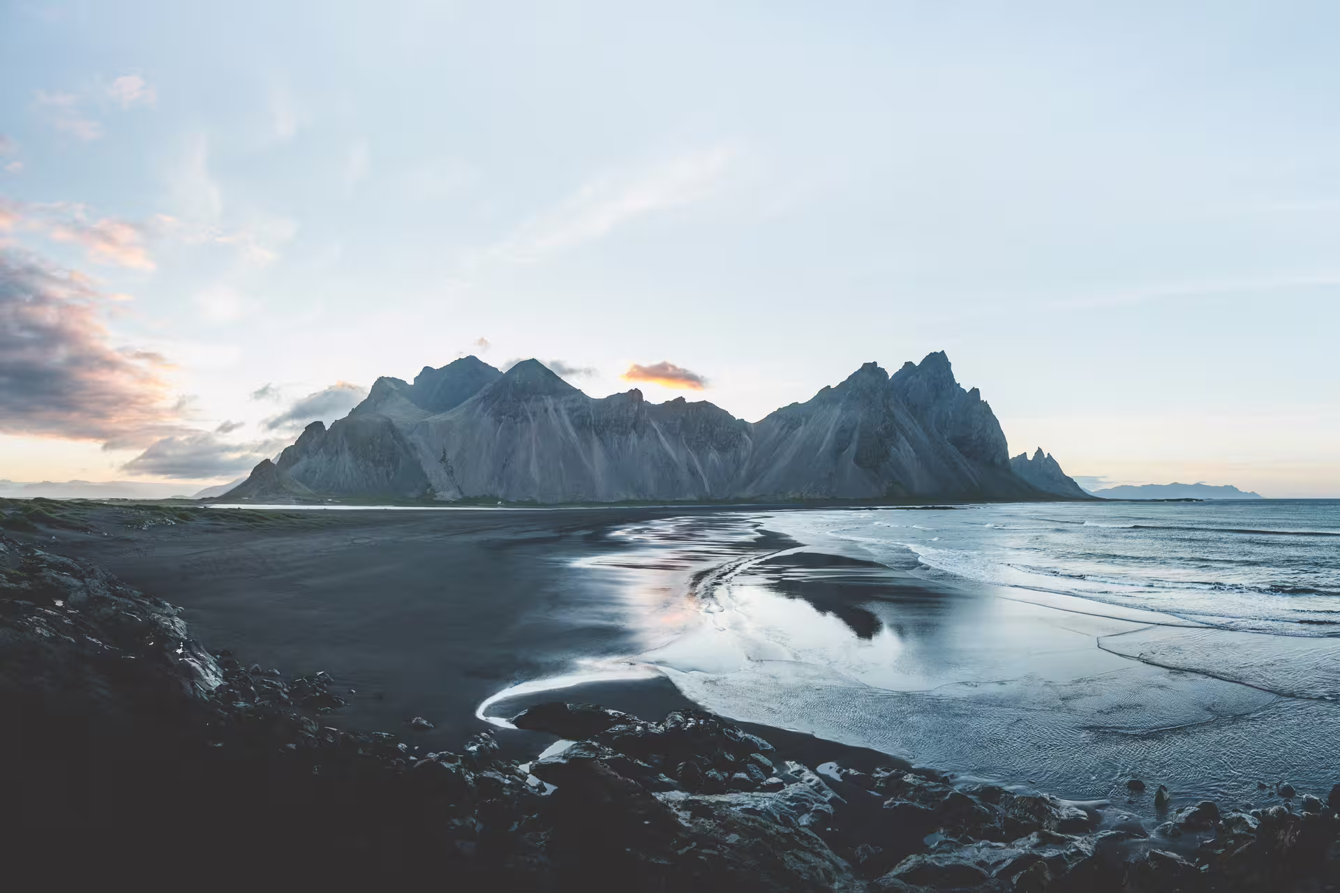 Black sand beach with reflective tidal flats and dramatic jagged mountains at twilight in Iceland