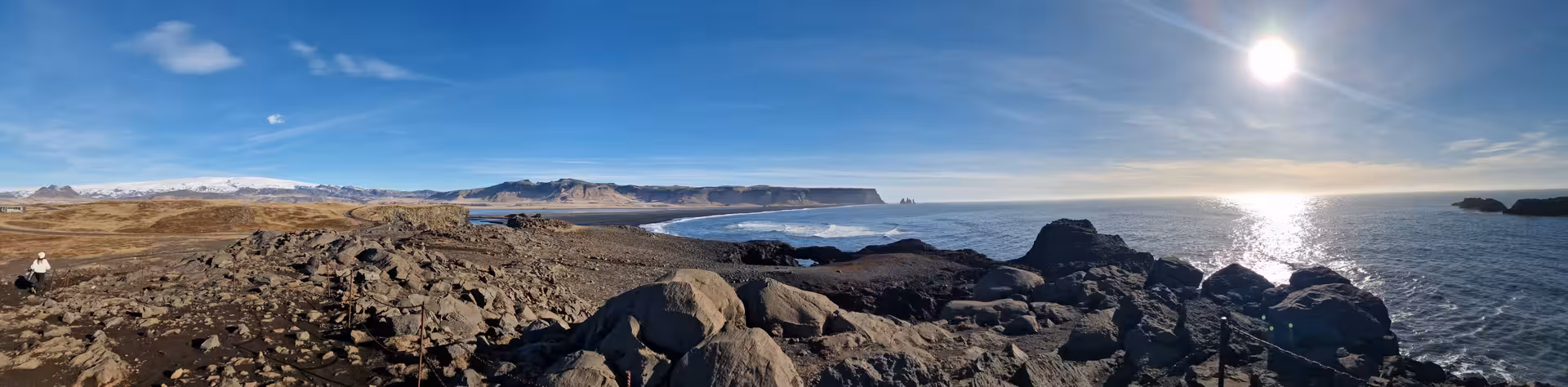 Panoramic view of Iceland's black sand beach coastline with volcanic rocks, ocean, and snow-capped mountains